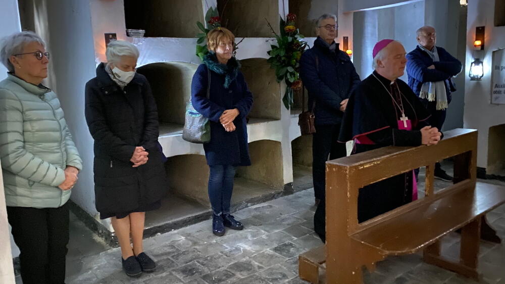 Hulpbisschop De Jong in gebed met vier personen op de achtergrond in de crypte